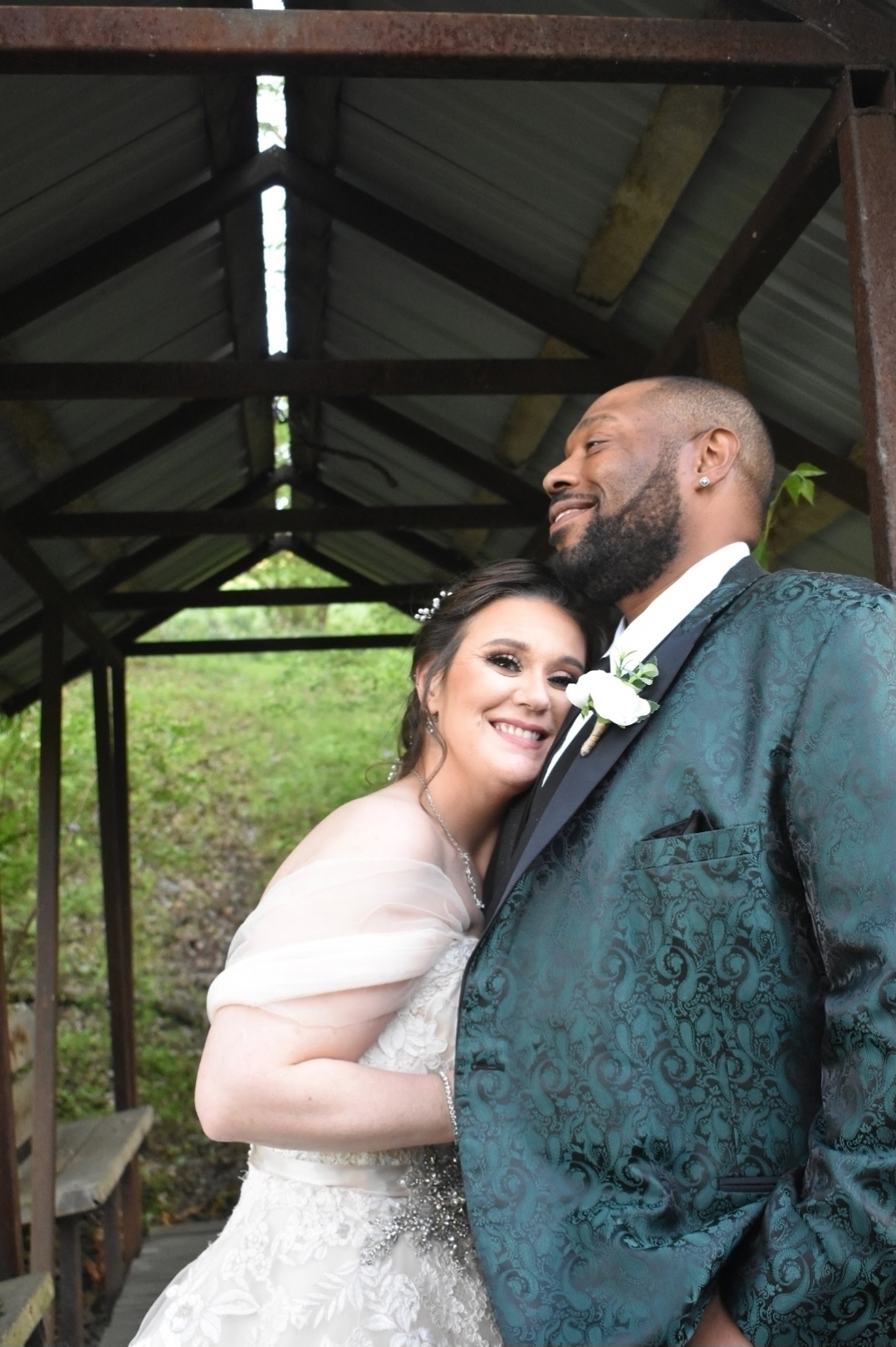 Bride and groom photographed on a bridge, groom wearing a green suit